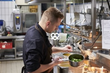 Koch in Gastronomieküche mit Kasserole in der Hand.