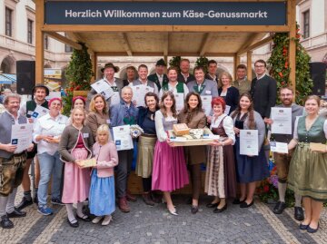 Gruppenfoto der Gewinner des Käsewettbewerbs 2025: eine Gruppe von Menschen in bayerischer Tracht, einige halten Urkunden, einige halten Holzbretter mit Käse