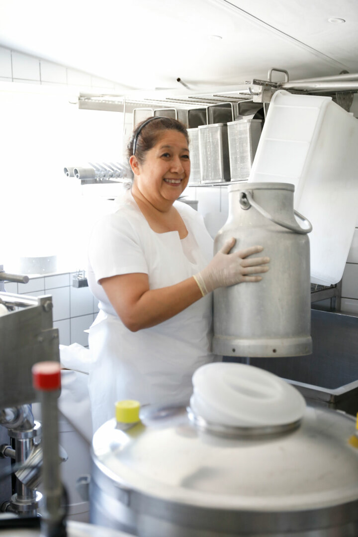 Frau in Käseküche mit Milchkanne in den Händen.